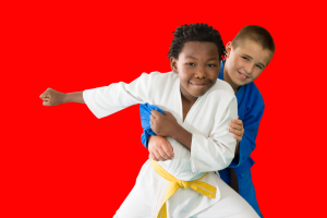 1 boy in white karate uniform. 1 boy in Blue karate uniform grappling. Red background 